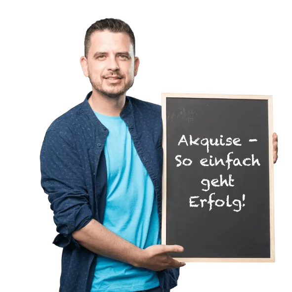 Mann hält eine Tafel mit der Aufschrift "Akquise - So einfach geht Erfolg" im Arm. Er trägt ein blaues T-Shirt und eine dunkelblaue Jacke.
